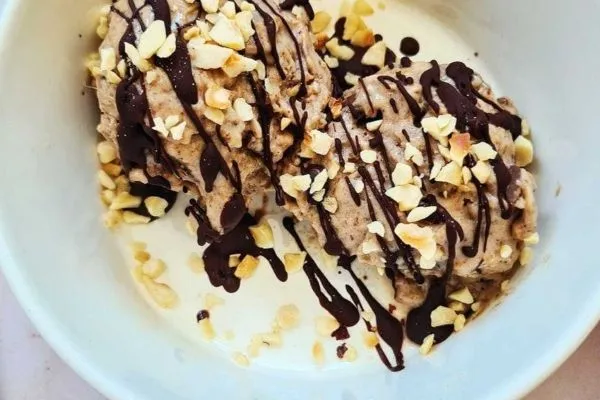 Bowl of banana flavored ice cream covered in chocolate sauce and crushed almonds